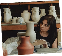 A female artist shaping clay on a potter's wheel in a sunlit studio with natural light illuminating her workspace.